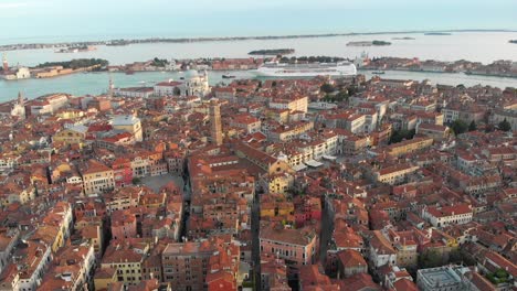 En-Venecia,-Italia,-El-Dron-Gira-A-La-Izquierda-Mientras-Se-Mueve-Por-El-Cielo-Sobre-Cientos-De-Edificios-Y-Destaca-Un-Crucero