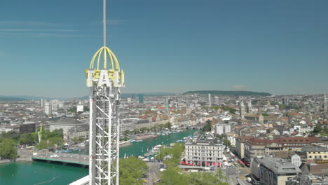Aerial-drone-shot-flyby-around-amusement-park-free-fall-tower-with-the-city-and-lake-of-Zürich,-Switzerland-in-the-background-during-Zürichfest