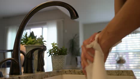 Young-man-dries-clean-hands-with-paper-towel-at-modern-kitchen-sink