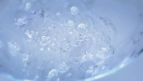 Slow-Motion---Shot-of-t-water-poured-into-a-glass-with-ice-cubes-with-a-light-blue-and-white-background