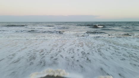 Establishing-shot-flying-into-beach-at-sunset-with-waves-crashing-in
