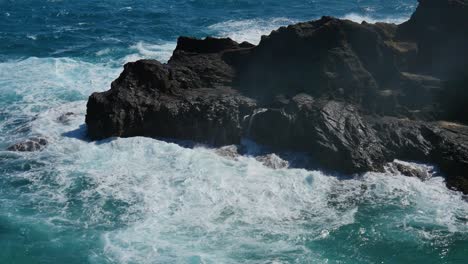 The-large-Pacific-surf-crashes-against-black-volcanic-rock-cliffs-on-Oahu-Hawaii-and-the-Pacific-is-a-beautiful-turquoise-in-the-sunlight