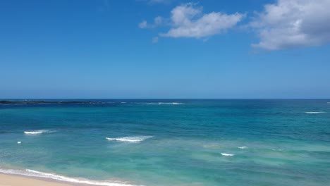 Rising-shot-of-property-directly-next-to-the-beach-on-north-shore-oahu-hawaii-with-blue-sky-turquoise-pacific-ocean-and-palm-trees-and-some-white-clouds