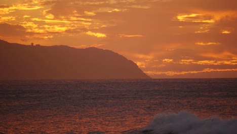 A-ave-rolls-in-as-the-sun-sets-over-Kaena-Point-Hawaii-Oahu-North-Shore-with-purple-and-orange-as-the-predominant-colours