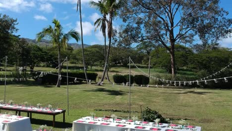rising-drone-shot-showing-tables-laid-for-wedding-dinner-supper-meal-in-hawaii-outdoors-with-lighting-and-wind-blowing-white-table-cloths-with-blue-sky-and-some-white-clouds