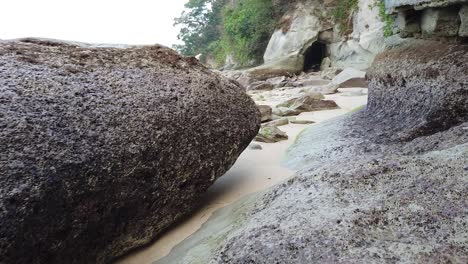 The-rocks-on-the-beach-at-low-tide-are-large-boulders-from-ancient-volcanic-eruptions-with-a-mysterious-cave-in-the-background