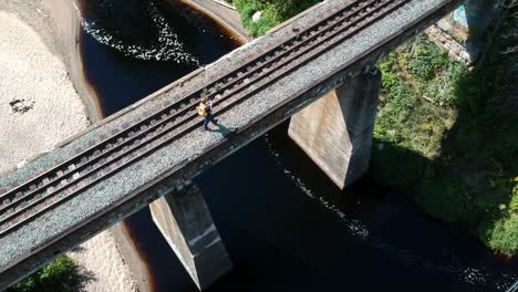 Drone-shot-of-man-walking-on-traintracks-with-a-strean-underneath-the-bridge-in-Canada