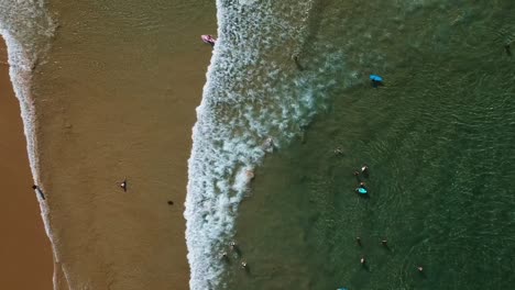 Drone-birds-eye-view-of-ocean-waves,-the-beach-and-surfing-in-crystal-clear-water