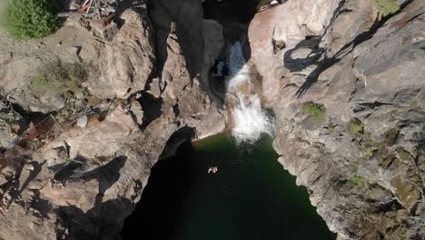 Young-man-slo-mo-cliff-jump-into-deep-green-pool-below-waterfall