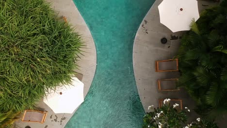 Top-down-bird's-eye-view-drone-shot-revealing-an-hourglass-shaped-pool-at-a-luxurious-resort-located-in-Bali,-Indonesia