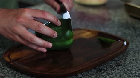 Cutting-and-removing-the-seeds-on-a-green-bell-pepper-on-a-wooden-cutting-board