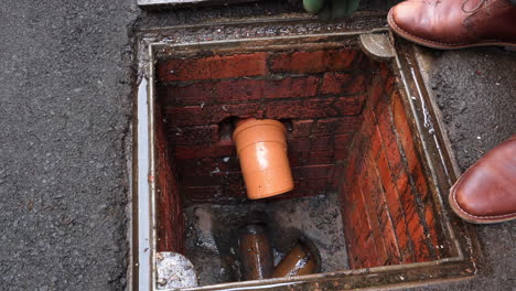 Inspecting-drain-sewer-man-with-gloves-on-points-to-problem-at-open-manhole