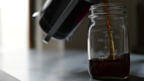 Woman-pours-coffee-from-french-press-into-mason-jar