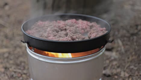 Minced-meat-cooking-in-a-frying-pan-on-top-of-a-camping-stove,-stationary-shot