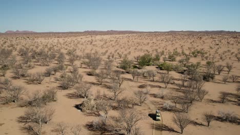 Safari-truck-drives-on-dirt-track-through-drought-resistant-trees,-Namibia