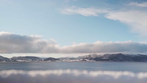Flauschige-Weiße-Wolken-über-Ruhigem-Meer-Und-Bergkette-Im-Winter
