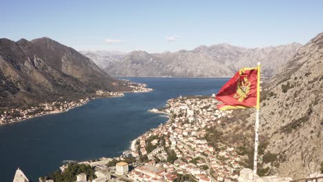 AERIAL---Bay-of-Kotor-and-national-flag,-Kotor,-Montenegro,-reverse-shot