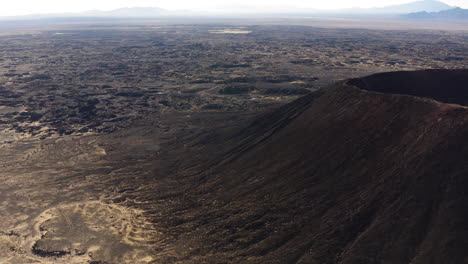 Drone-Cerca-Del-Cráter-Amboy-Inactivo-Volcán-De-Cono-De-Ceniza-Se-Eleva-Sobre-El-Campo-De-Lava-Formación-De-Roca-Geológica-En-El-Este-Del-Desierto-De-Mojave-Del-Sur-De-California-Durante-Un-Día-Soleado
