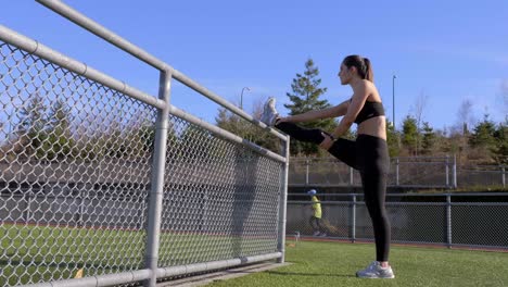 Athletic-young-woman-stretching-leg-against-railing-before-run