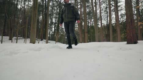 Static-shot-of-Day-Hiker-Walking-towards-camera-with-Backpack-through-Snow-Covered-Winter-Forest