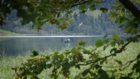 Man-fishing-while-standing-alone-on-speed-boat-on-a-huge-lake-surrounded-by-trees
