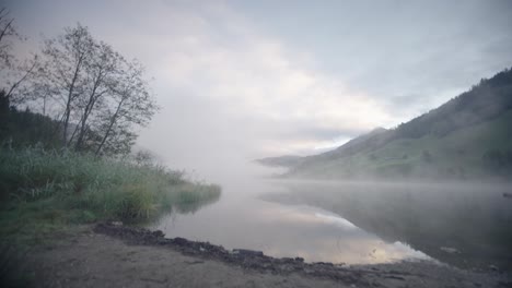 Upwards-dolly-shot-revealing-lake-covered-in-misty-fog-at-dawn-or-dusk