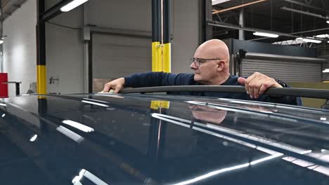 Bald-person-cleaning-rooftop-of-black-vehicle-inside-modern-garage,-slow-motion-shot