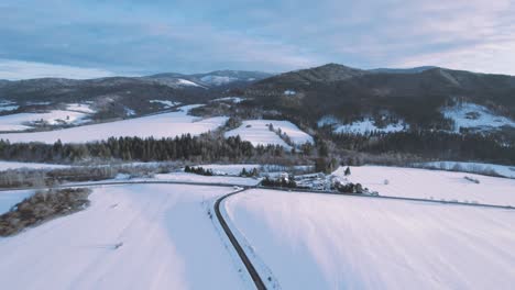Scenic-drone-aerial-view-parallel-to-lonely-road-in-middle-of-snowy-mountain-scenery-in-Slovakia,-Banska-Bystrica,-Brezno