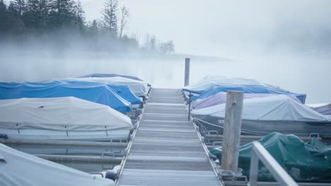 boats-docked-at-pier-on-misty-foggy-lake,-mountains-in-background