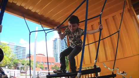 A-happy-young-boy-reaches-out-and-climbs-across-a-rope-swing-in-an-industrial-playground
