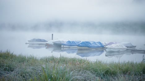 right-smooth-dolly-reveal-boats-docked-at-pier-on-misty-foggy-lake,-mountains-in-background