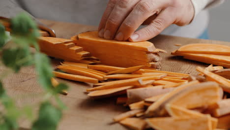 Male-chef-sliceing-sweet-potato-in-thin-slices-for-sweet-potato-fries-in-the-kitchen-on-a-wooden-cutting-board-in-the-kitchen