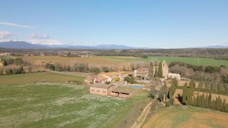 Aerial-view-of-nature-sown-field-without-people-Snowy-Pyrenees-mountain-in-the-background-Small-church-with-growing-olive-trees-in-front