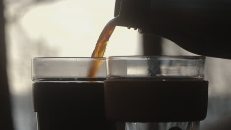 Pouring-steaming-hot-coffee-from-a-thermos-flask-into-a-sustainable-keep-cup-out-of-glass