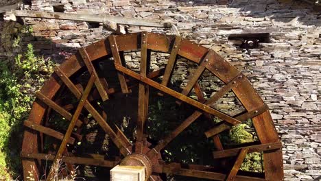 Big-water-wheel-rotating-fast,-attached-to-an-old-stone-house