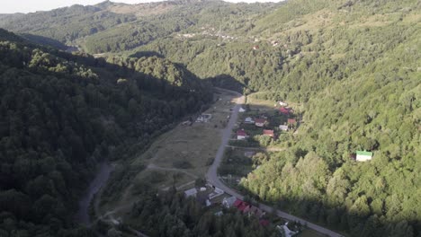 Aerial-view,-flying-forward-above-a-little-romanian-town-between-two-green-mountains-covered-in-dense-forest-at-daylight