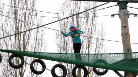 Young-girl-walking-across-tyres-on-ropes-on-a-high-wire-adventure-obstacle-course