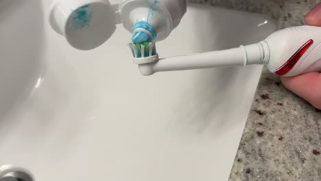 Allgemeine-Aufnahme-Einer-Weißen-Kaukasischen-Hand,-Die-Zahnpasta-Auf-Eine-Elektrische-Zahnbürste-Aufträgt-Und-Sich-Auf-Das-Zähneputzen-Vorbereitet