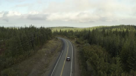 Drone-shoot-of-a-Grey-Car-driving-on-a-road-in-the-middle-of-a-forest-on-a-cloudy-day-in-4k