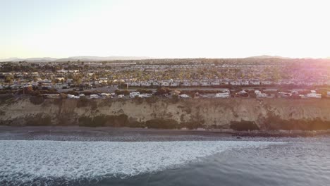 A-beautiful-aerial-drone-shot,-drone-ascending-and-revealing-a-town-with-palm-treetops-and-mountains-in-the-background,-Carlsbad-State-Beach---California