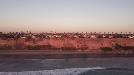 A-beautiful-aerial-drone-shot,-drone-flying-backwards-out-to-the-ocean-with-a-view-of-the-horizon-and-landscape,-Carlsbad-State-Beach---California