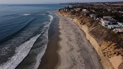 A-stunning-aerial-drone-shot,-flying-along-the-coastline-over-the-beach,-Solana-Beach---San-Diego---California