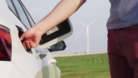 Opening-car-gas-tank-cap,-windmill-in-background,-change-from-fossil-fuel-to-electric-power