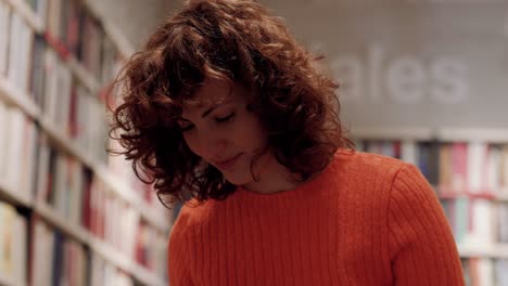 Focused-Caucasian-Curly-Woman-Studying-Among-Book-Shelves-In-Library