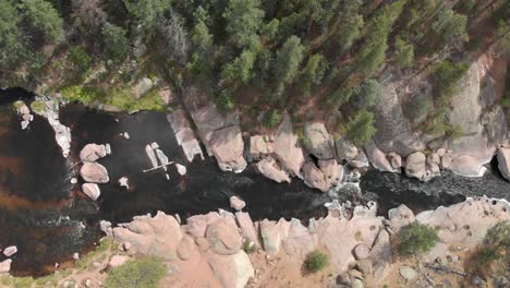 Low-vertical-aerial-of-shallow-rocky-river-running-through-forest