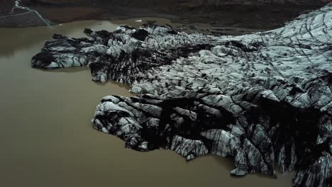 Aerial-view-over-Sólheimajökull-glacier,-melting-into-dark-water,-in-summer,-Iceland