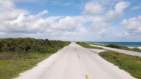 Low-angle-drone-shot-of-a-young-women-driving-a-red-scooter-down-a-highway-along-the-ocean-located-on-the-tropical-island-of-Cozumel,-Mexico-shot-in-4k