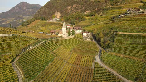 Aerial-Drone-Over-a-medieval-church-in-the-middle-of-the-Vineyards-in-Autumn-in-South-Tyrol,-St