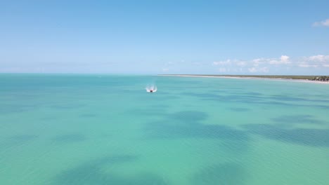Wide-angle-drone-shot-approaching-a-boat-going-past-the-frame-driving-on-the-crystal-clear-blue-waters-off-the-coast-of-the-tropical-island-of-Holbox-in-Mexico-shot-in-4k