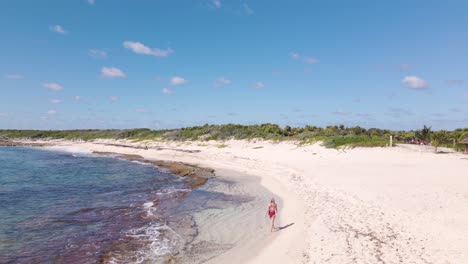 Wide-angle-drone-shot-of-a-beautiful-young-caucasian-women-walking-down-the-white-sandy-beaches-on-the-tropical-island-of-Cozumel-in-Mexico-shot-during-a-hot-sunny-day-in-4k
